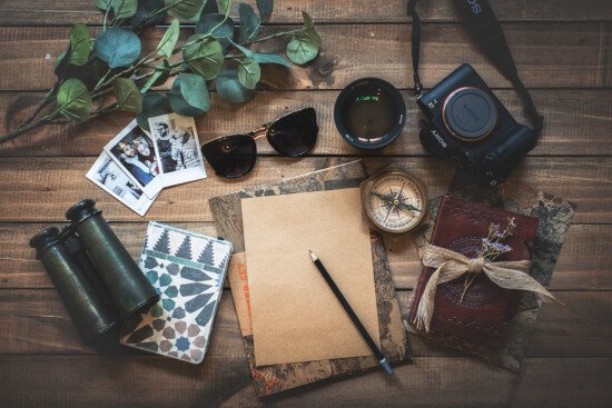 Wichtige Gegenstände für einen nachhaltigen Urlaub: Kamera, Papier, Fotos, Sonnenbrille und Fernglas