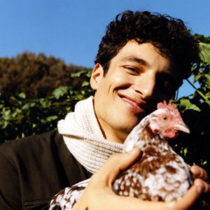 Mann trägt vegane Mode und hält glückliches Huhn in den Händen